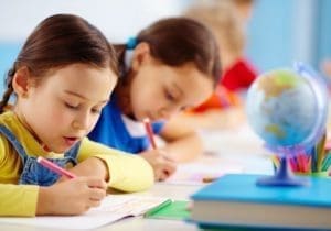 Young students writing in a classroom with a globe on the desk at KidAble. โปรแกรมการพัฒนาแบบมอนเตสซอรีสำหรับเด็ก